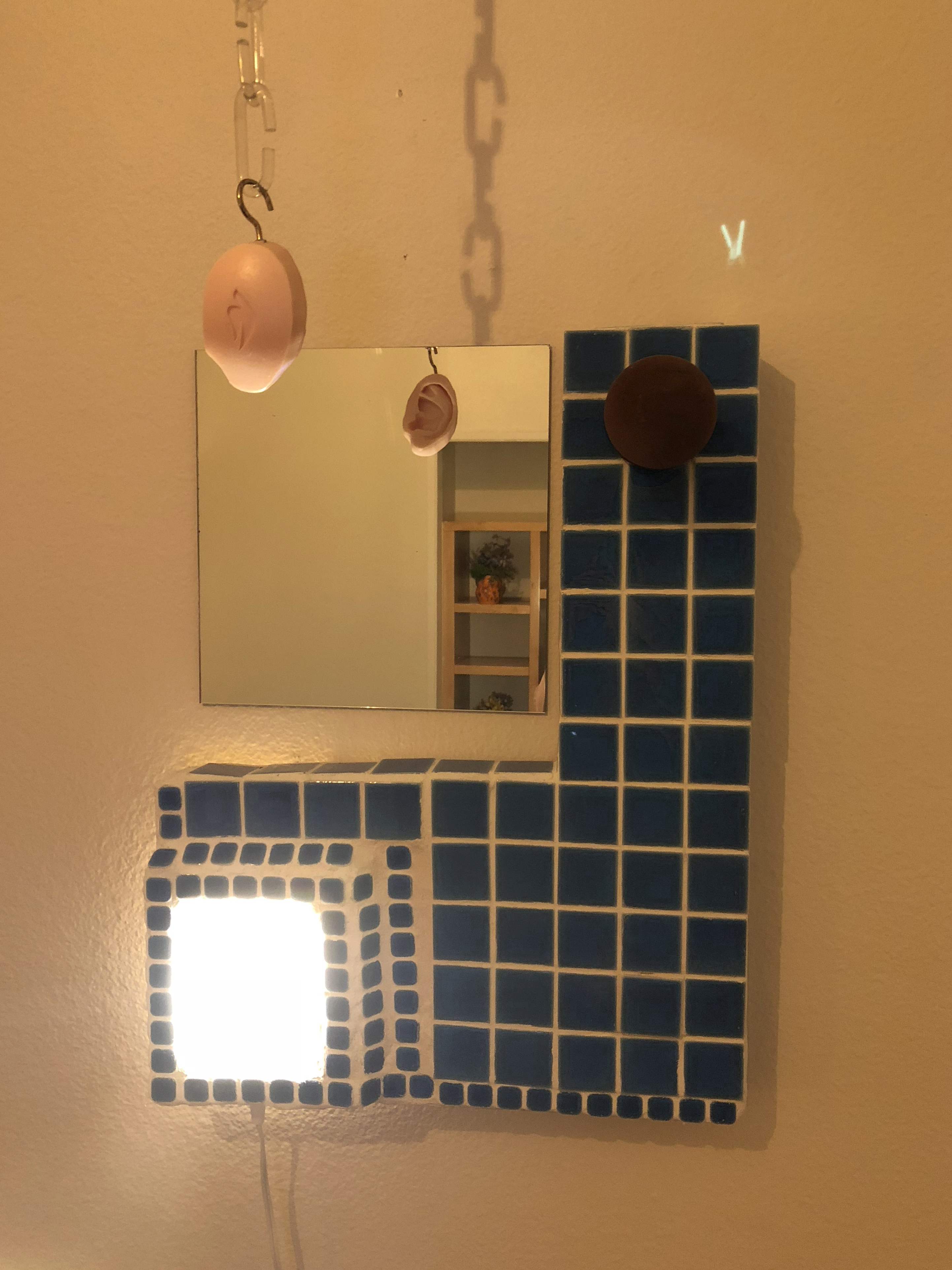 Detail of a sculptural wall lamp made of tile and mirror with a soap sculpture hung in front of it